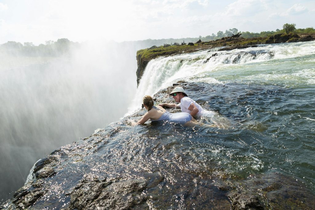 Man and a girl in water of the Devil's Pool on the edge of Victoria Falls.